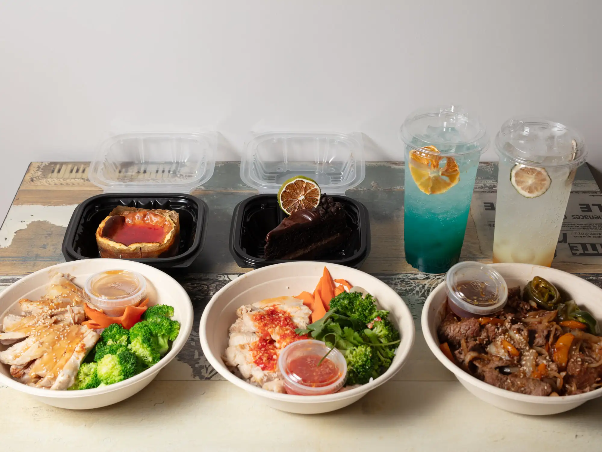 Three hibachi bowls, bento trays and a row of house drinks batched together on a pale wooden table