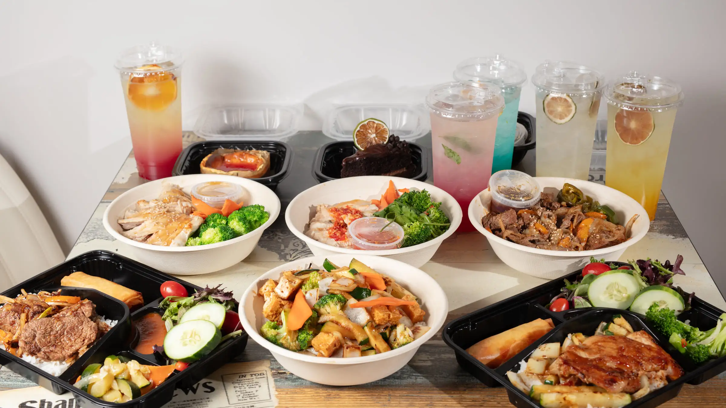A spread of hibachi bowls, bento trays and house drinks from Hibachi K and Sushi, laid out on a pale wooden table