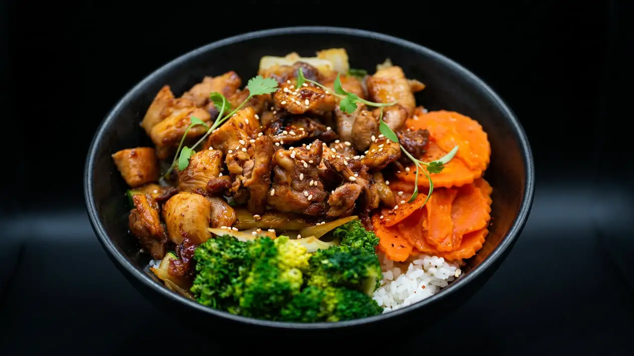 Teriyaki chicken with sesame seeds and cilantro in a black bowl, with broccoli, crinkle-cut carrots and onion over white rice